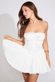 Model is wearing a white PLEATING DETAIL STRAPLESS RUFFLE HEM MINI DRESS with brown heels on a white background.
