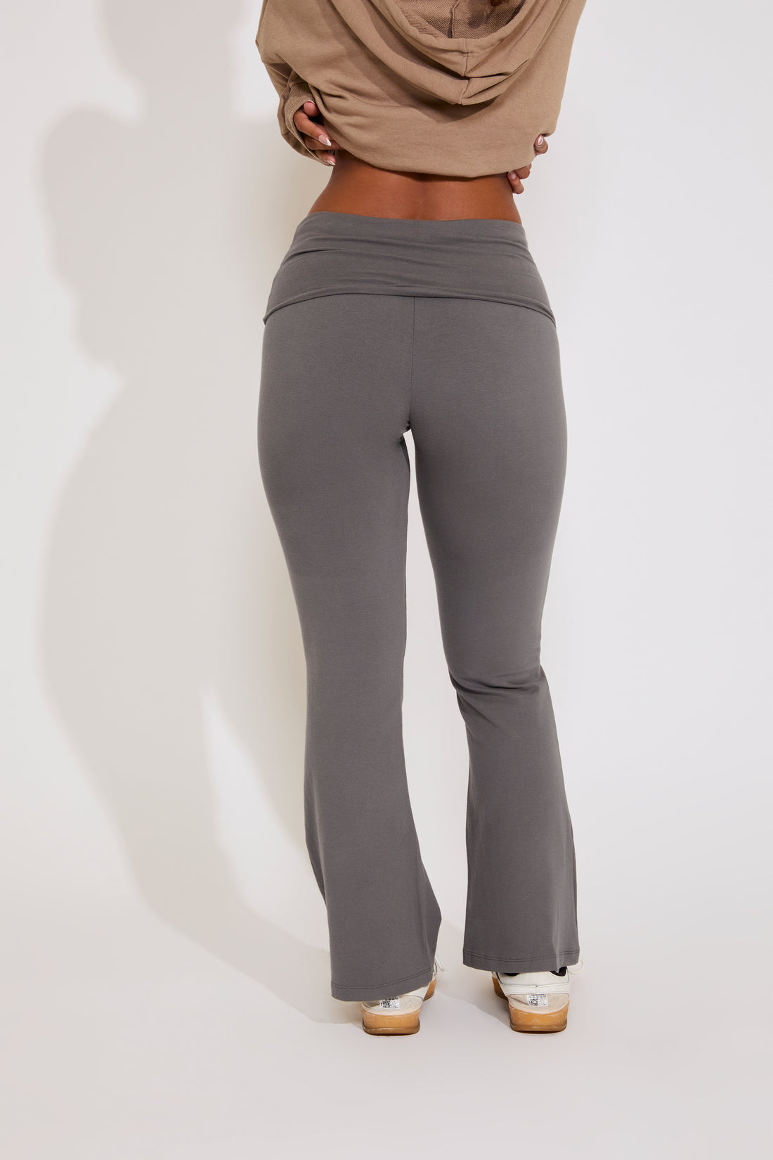 Person wearing gray flared pants and a beige top on a white background