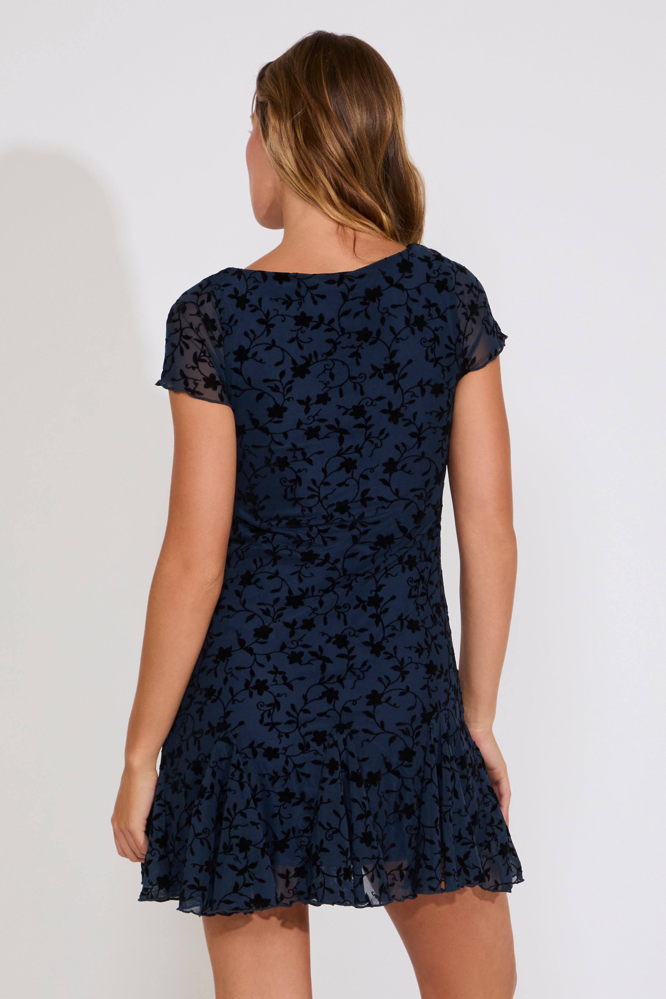 Woman wearing a navy blue dress with black floral pattern on a white background