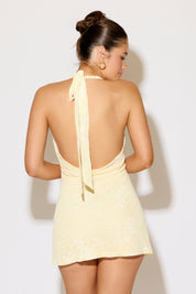 Woman wearing a light yellow dress with a halter neck and open back on a white background