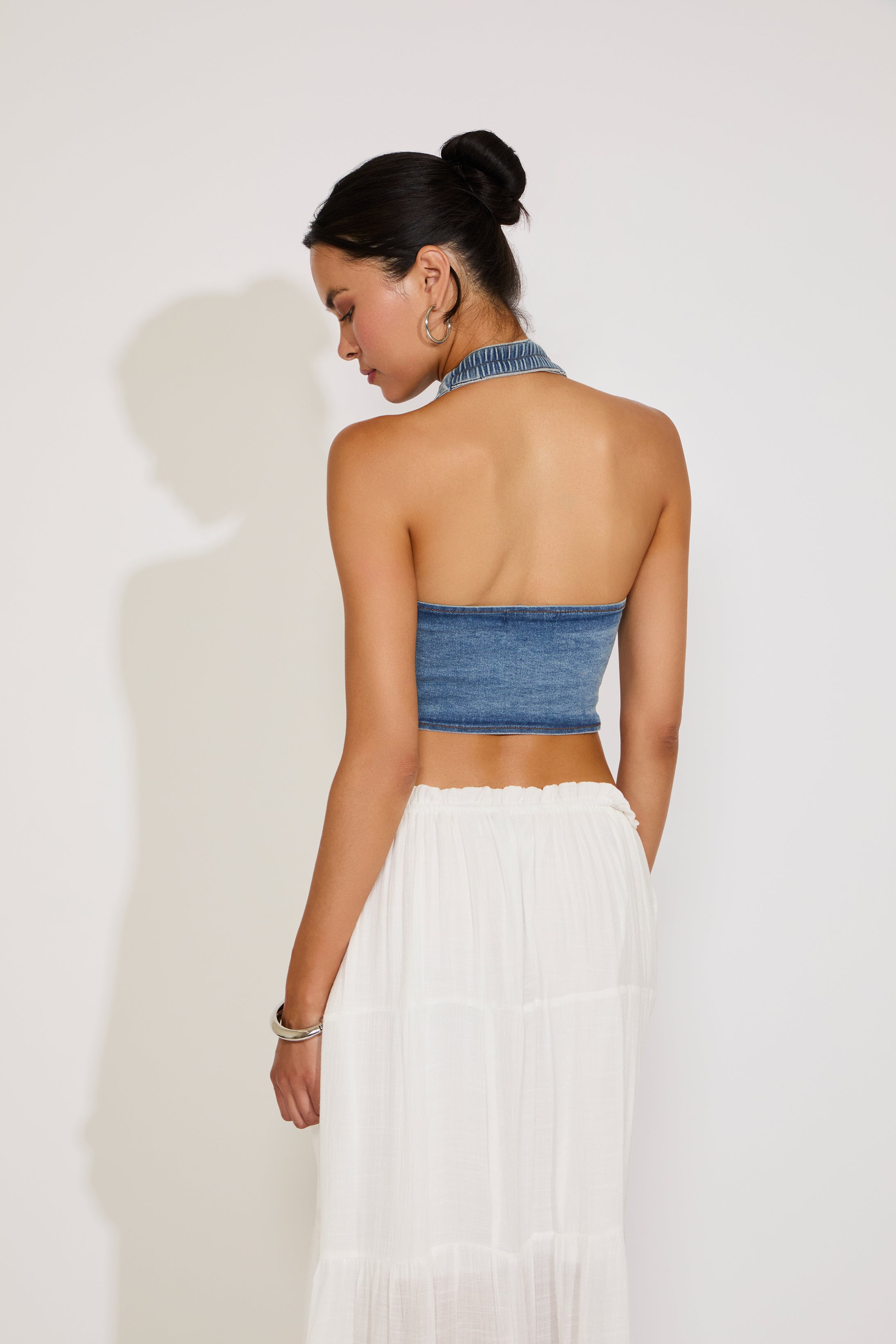 Woman wearing a blue strapless top and white skirt on a plain background