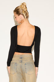 Person wearing a black long-sleeve top with an open back and beige pants on a white background