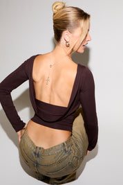 Woman wearing a long-sleeve top with an open back and high-waisted pants on a plain background