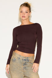 Woman wearing a brown long-sleeve top and beige pants against a white background