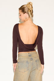 Woman wearing a brown open-back top and beige pants against a white background