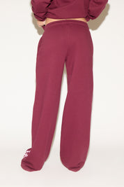 A woman poses against a white background wearing a burgundy cropped hoodie and matching wide-leg sweatpants with “Los Angeles” text down one leg.