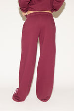 A woman poses against a white background wearing a burgundy cropped hoodie and matching wide-leg sweatpants with “Los Angeles” text down one leg.
