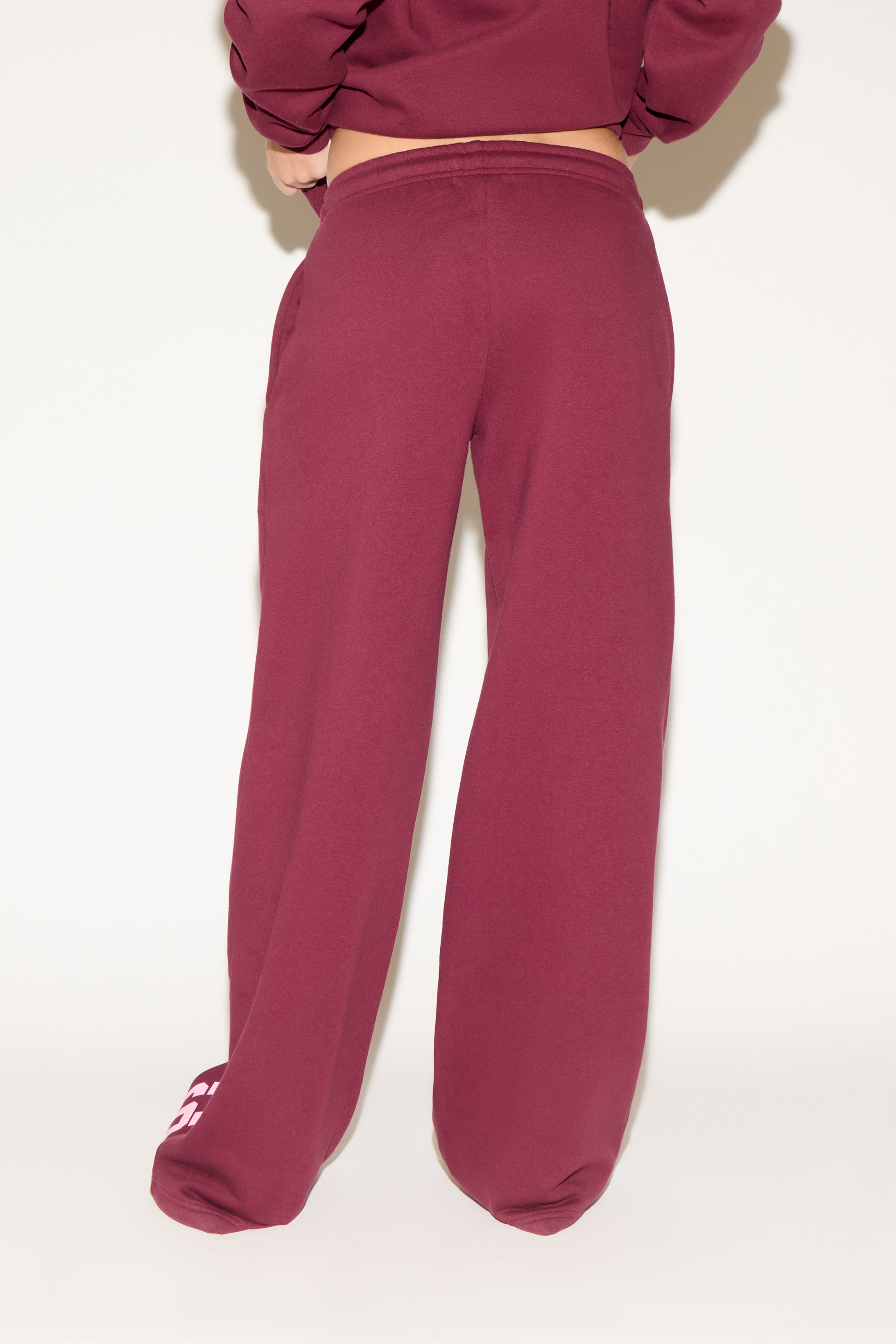 A woman poses against a white background wearing a burgundy cropped hoodie and matching wide-leg sweatpants with “Los Angeles” text down one leg.