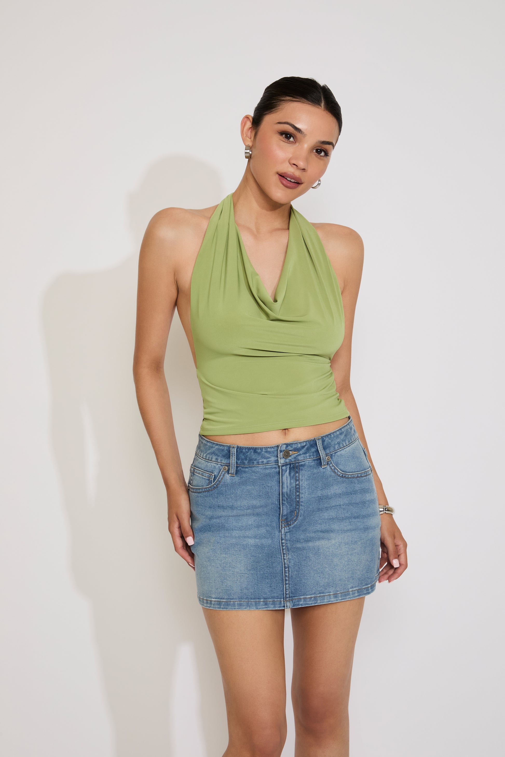 Woman wearing a green halter top and denim skirt against a white background