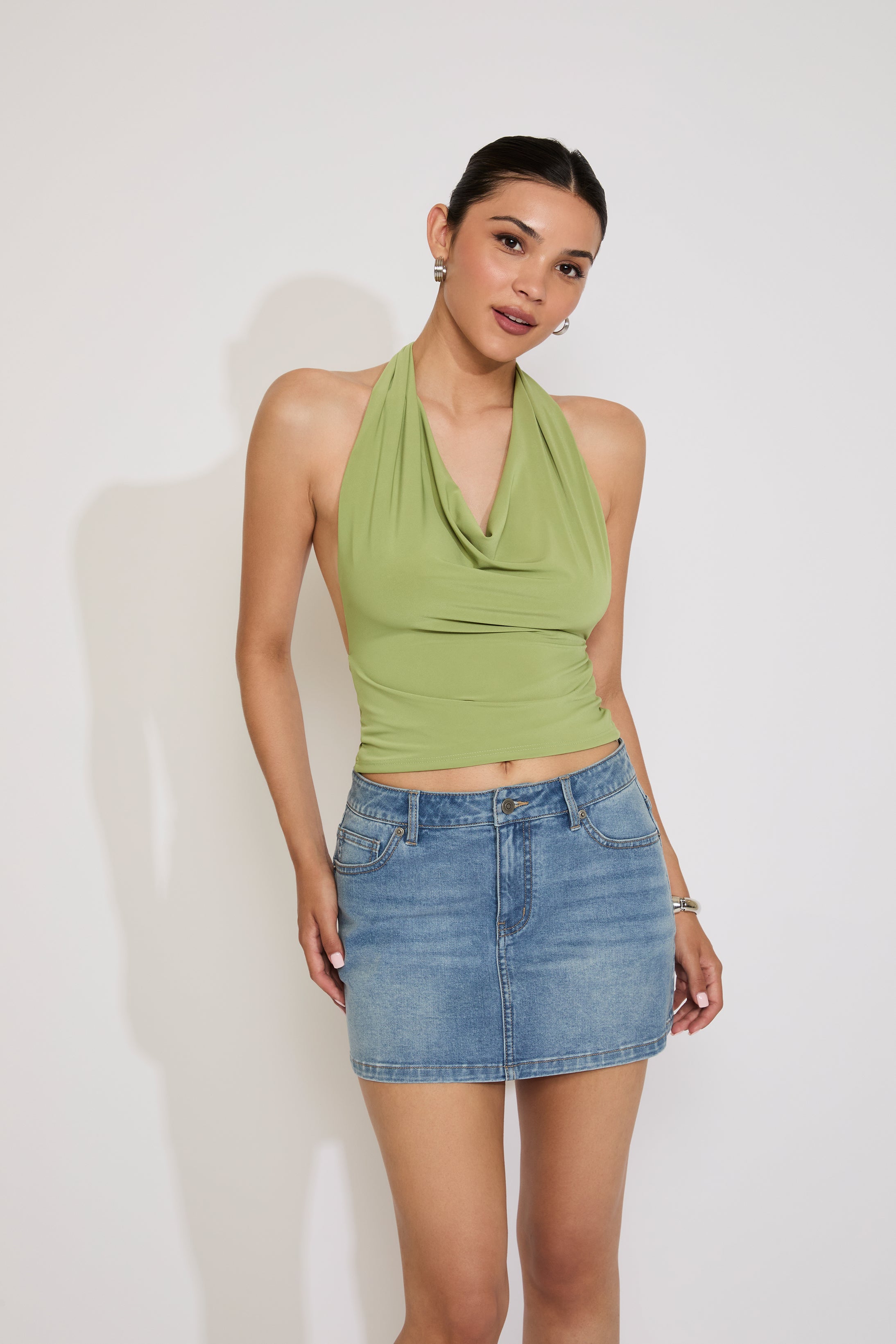 Woman wearing a green halter top and denim skirt against a white background