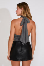 Woman wearing a gray halter top with a bow and black leather skirt on a white background
