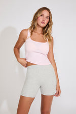 Woman wearing a pink tank top and gray shorts on a white background