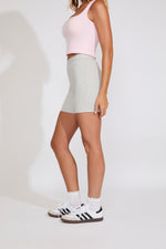 Person wearing a light pink crop top and gray skirt with white sneakers on a plain background