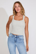 Woman wearing a light gray tank top and blue jeans against a plain background