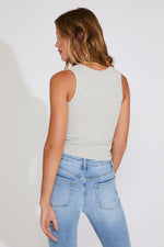 Woman wearing a light gray sleeveless top and blue jeans on a white background