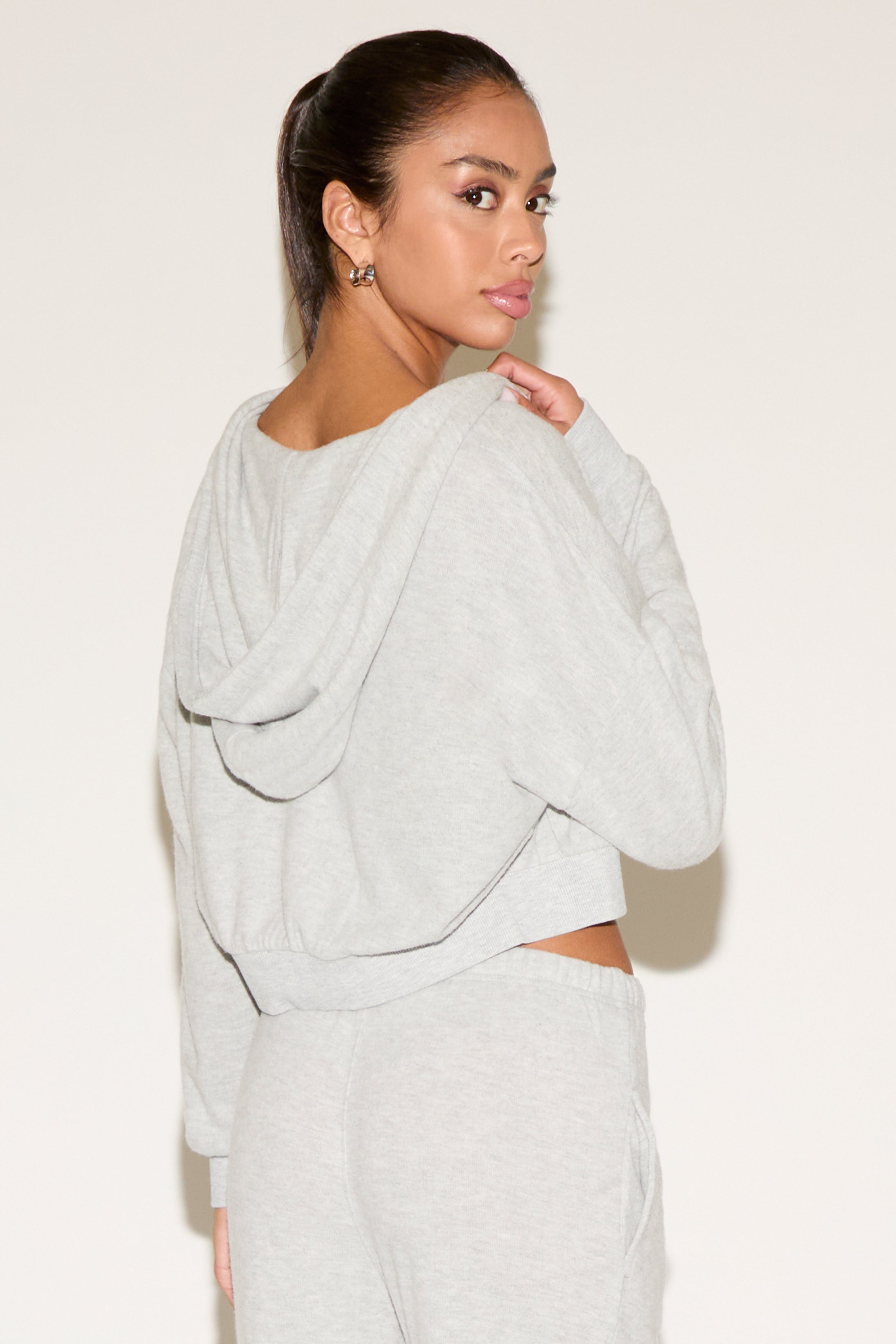 Woman wearing a light gray oversized sweater with a plain background