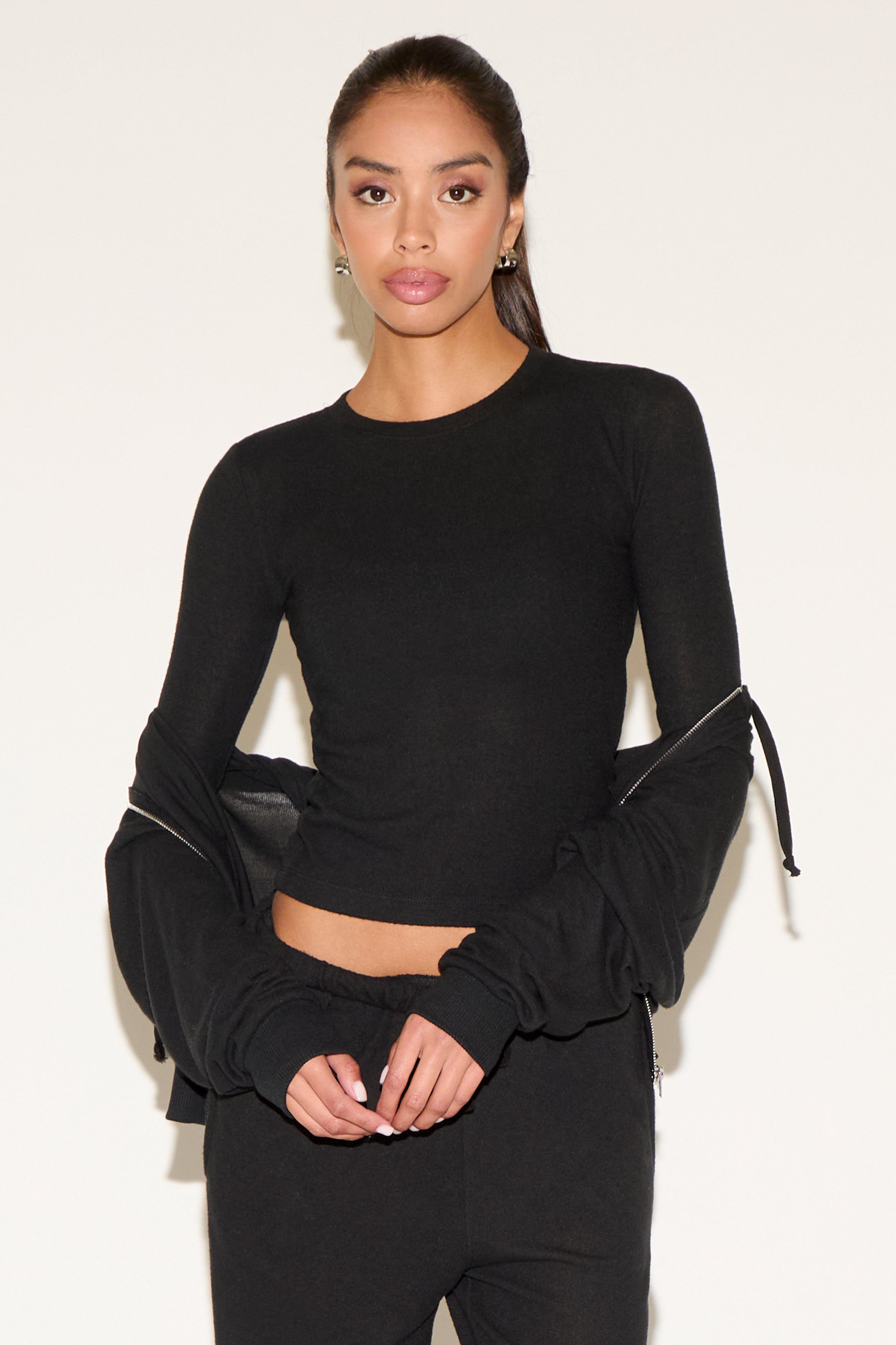 Woman wearing a black long-sleeve top with ruched sleeves against a white background