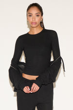 Woman wearing a black long-sleeve top with ruched sleeves against a white background