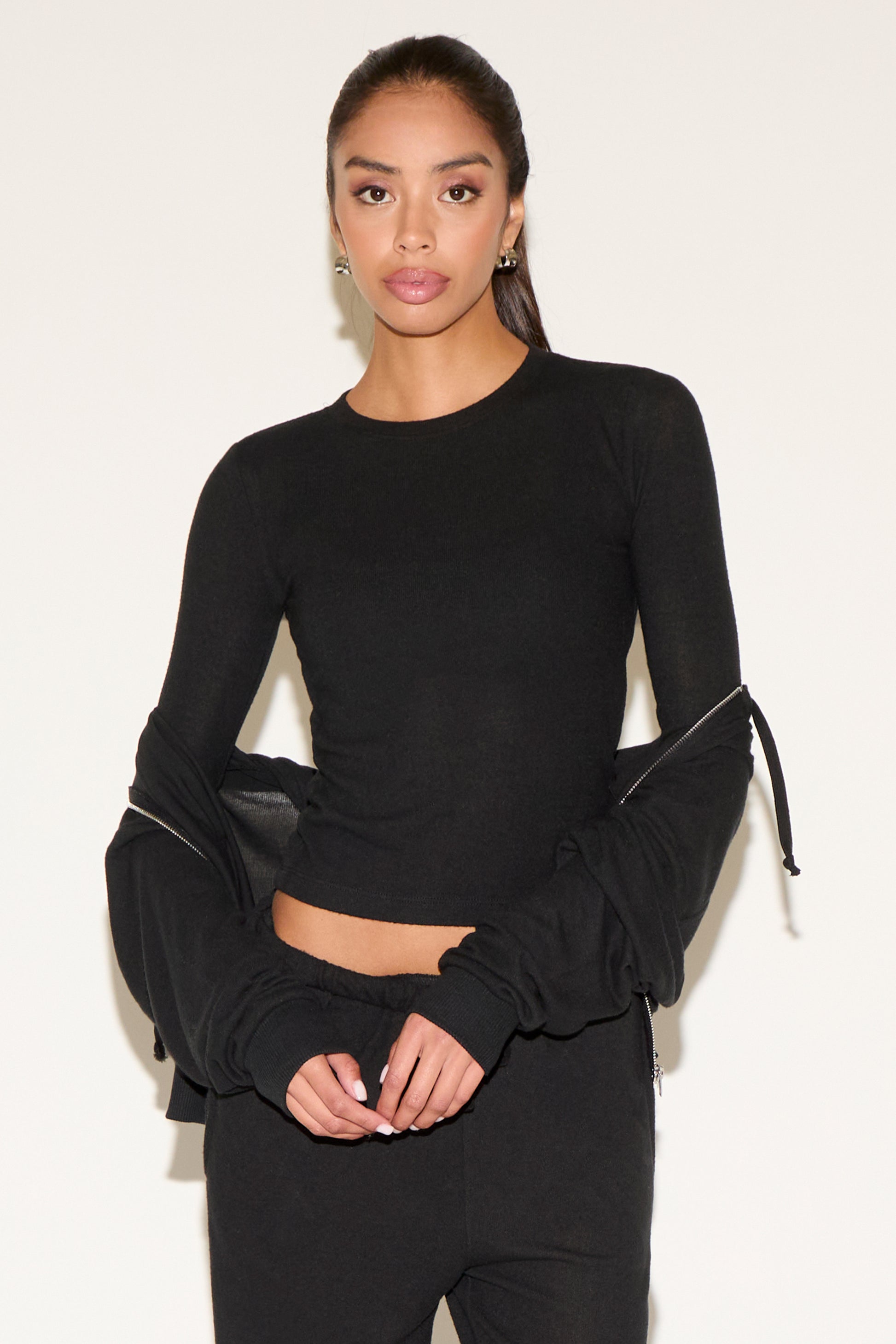 Woman wearing a black long-sleeve top with ruched sleeves against a white background