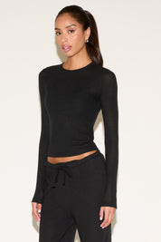 Woman wearing a black long-sleeve top and black pants against a white background