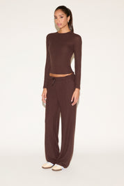 Woman wearing a brown long-sleeve top and wide-leg pants on a white background