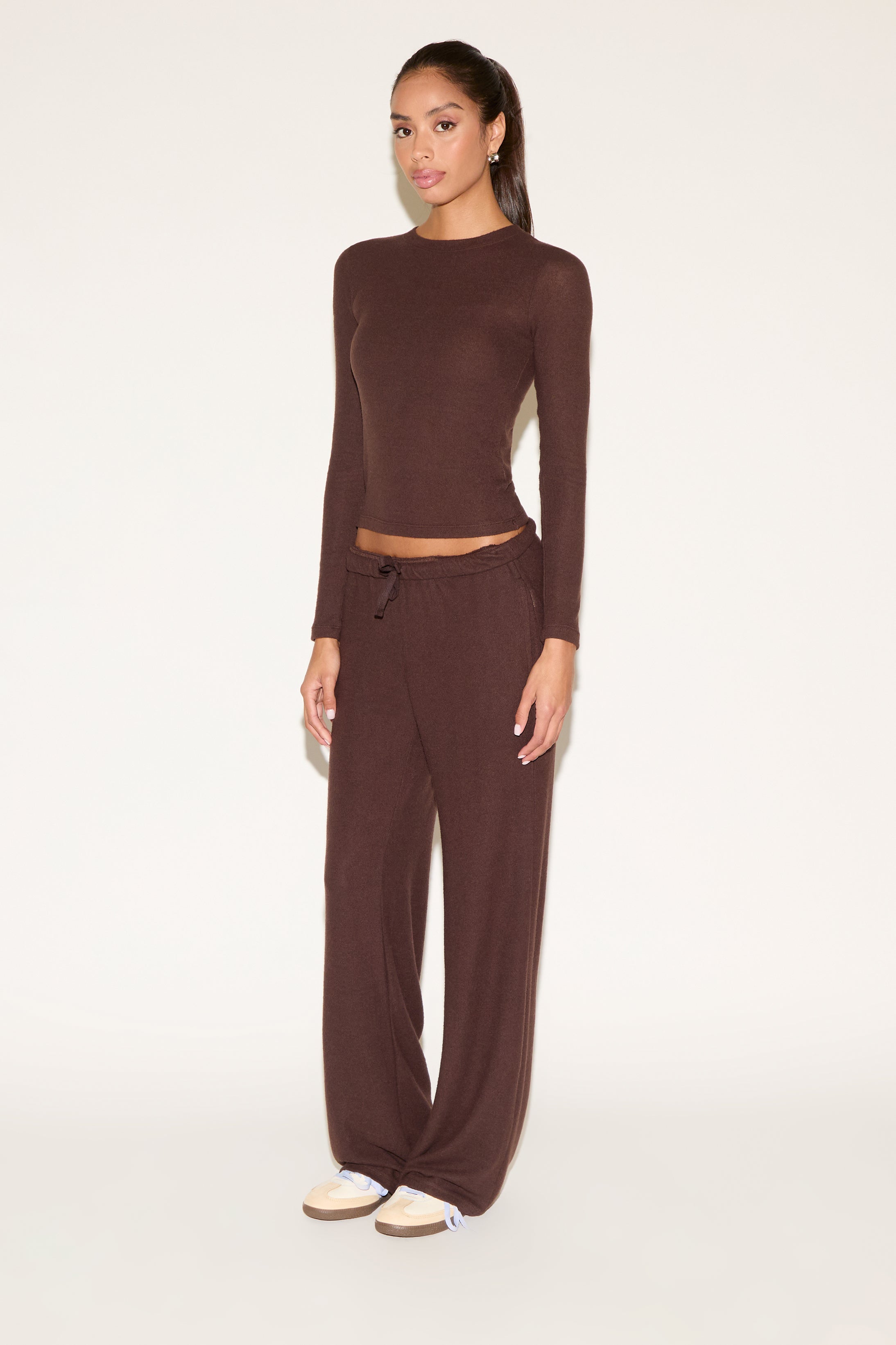 Woman wearing a brown long-sleeve top and wide-leg pants on a white background