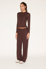 Woman wearing a brown long-sleeve top and wide-leg pants on a white background
