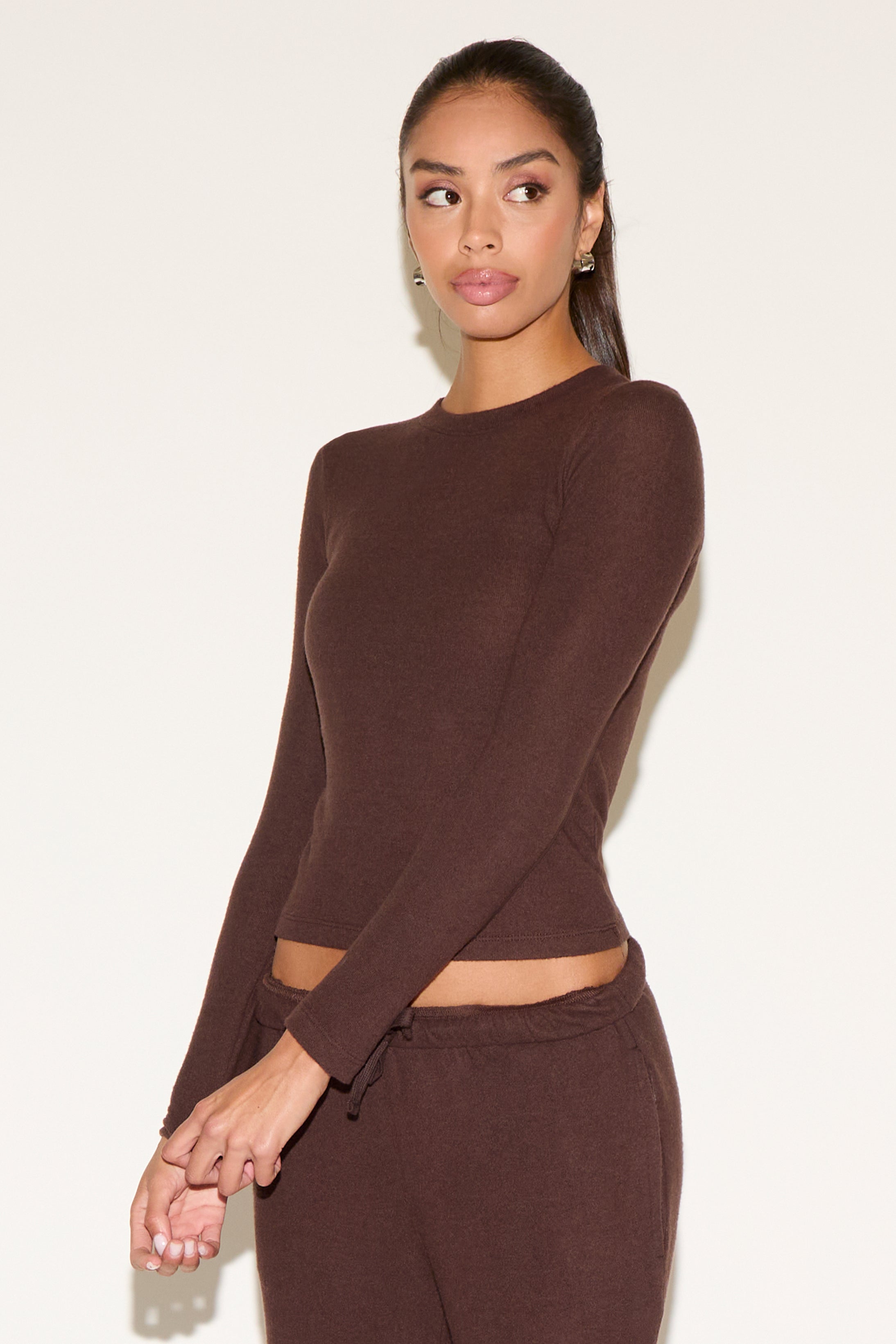 Woman wearing a brown long-sleeve top and pants against a white background