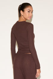 Woman wearing a brown long-sleeve top and pants against a white background