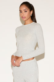 Woman wearing a gray long-sleeve top and white pants against a plain background