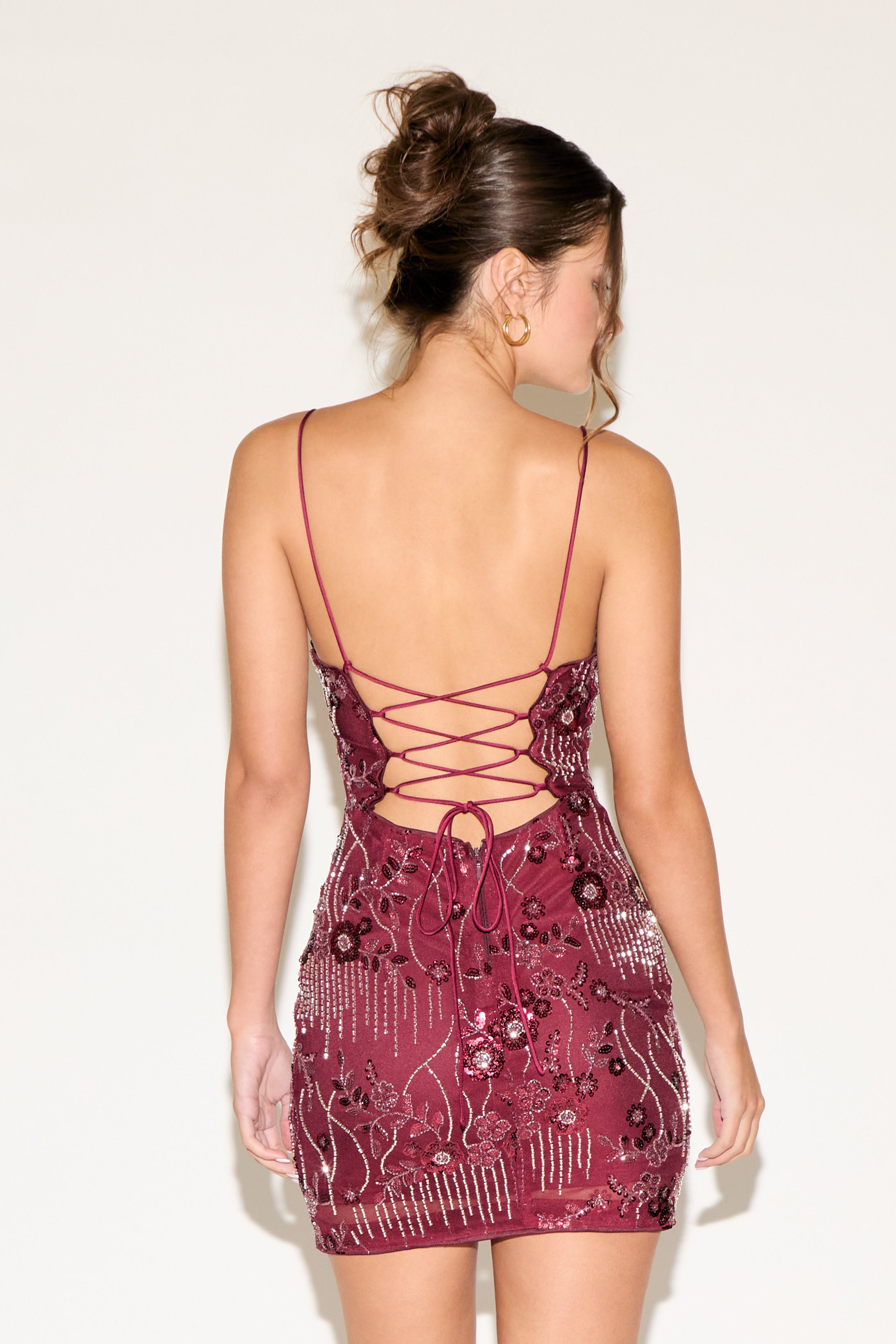 Woman wearing a patterned dress with thin straps and open back on a plain background