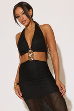 Woman wearing a black halter top with a gold accent and black skirt against a white background