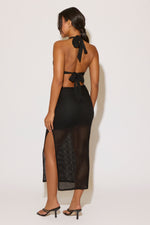 Woman wearing a black halter neck dress with mesh panels on a white background