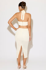 Woman wearing a white outfit with a high slit on a plain background