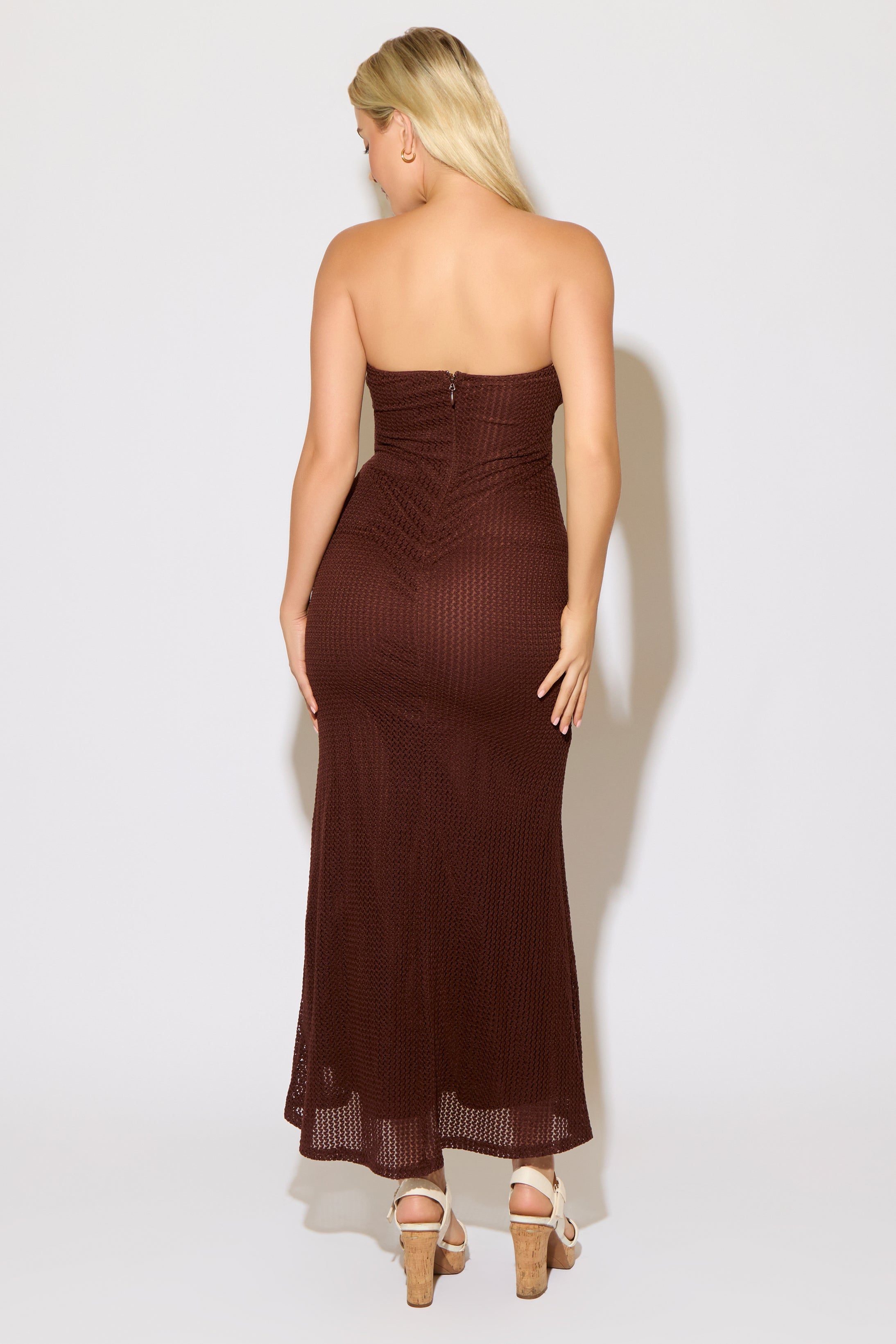 Woman wearing a strapless brown evening gown with a cutout design on a white background.
