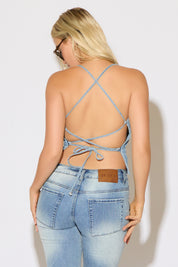 Model is wearing a cross tie back denim spaghetti strap top paired with denim jeans and sunglasses on a white back ground.