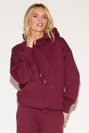 A woman poses against a white background wearing a burgundy cropped hoodie and matching wide-leg sweatpants. 