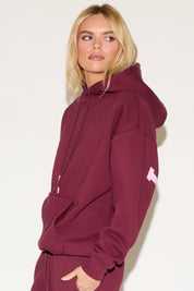 A woman poses against a white background wearing a burgundy cropped hoodie and matching wide-leg sweatpants. 