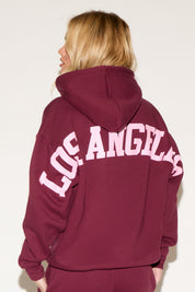 A woman poses against a white background wearing a burgundy cropped hoodie and matching wide-leg sweatpants. 