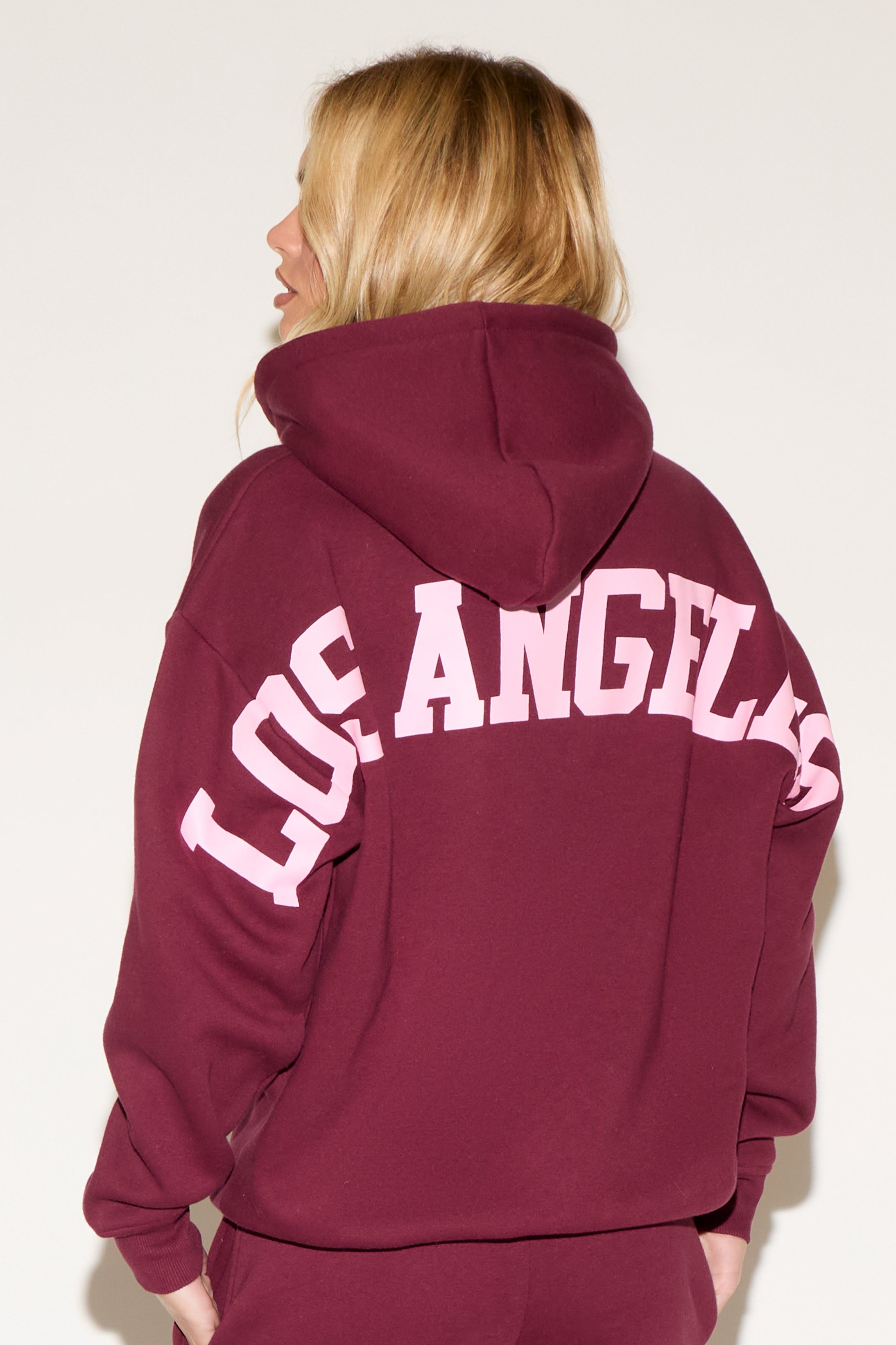 A woman poses against a white background wearing a burgundy cropped hoodie and matching wide-leg sweatpants. 