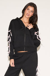 Woman wearing a black hoodie with white lace details on sleeves against a white background