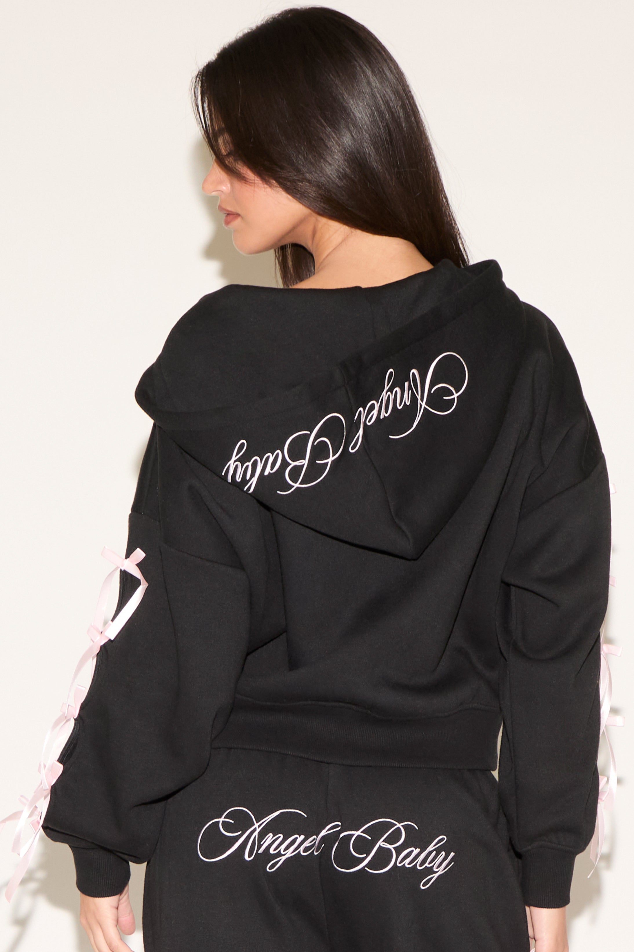 Person wearing a black hoodie with 'Angel Baby' text on the back against a white background