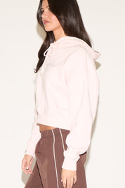 Woman wearing a light pink hoodie and brown pants on a white background