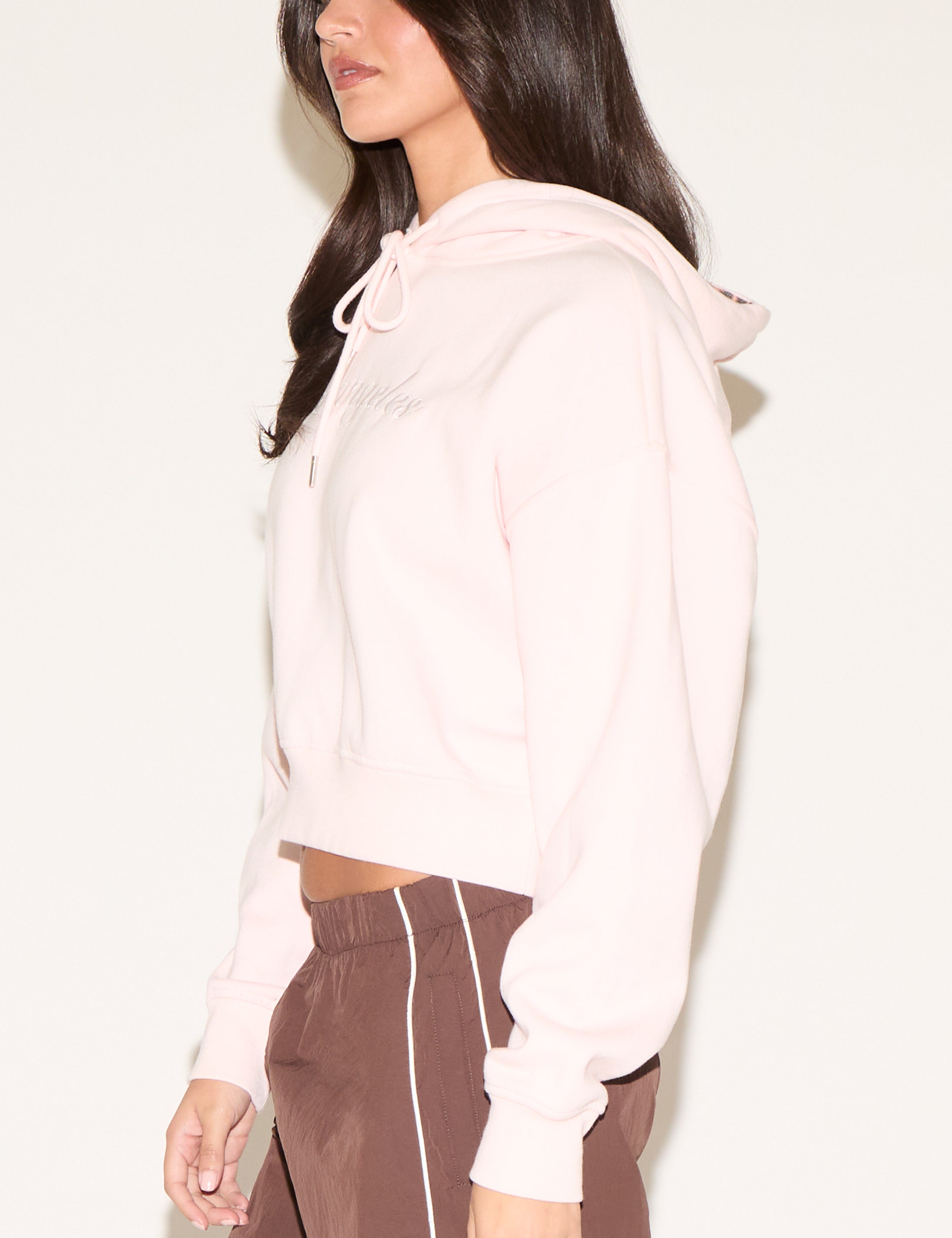 Woman wearing a light pink hoodie and brown pants on a white background