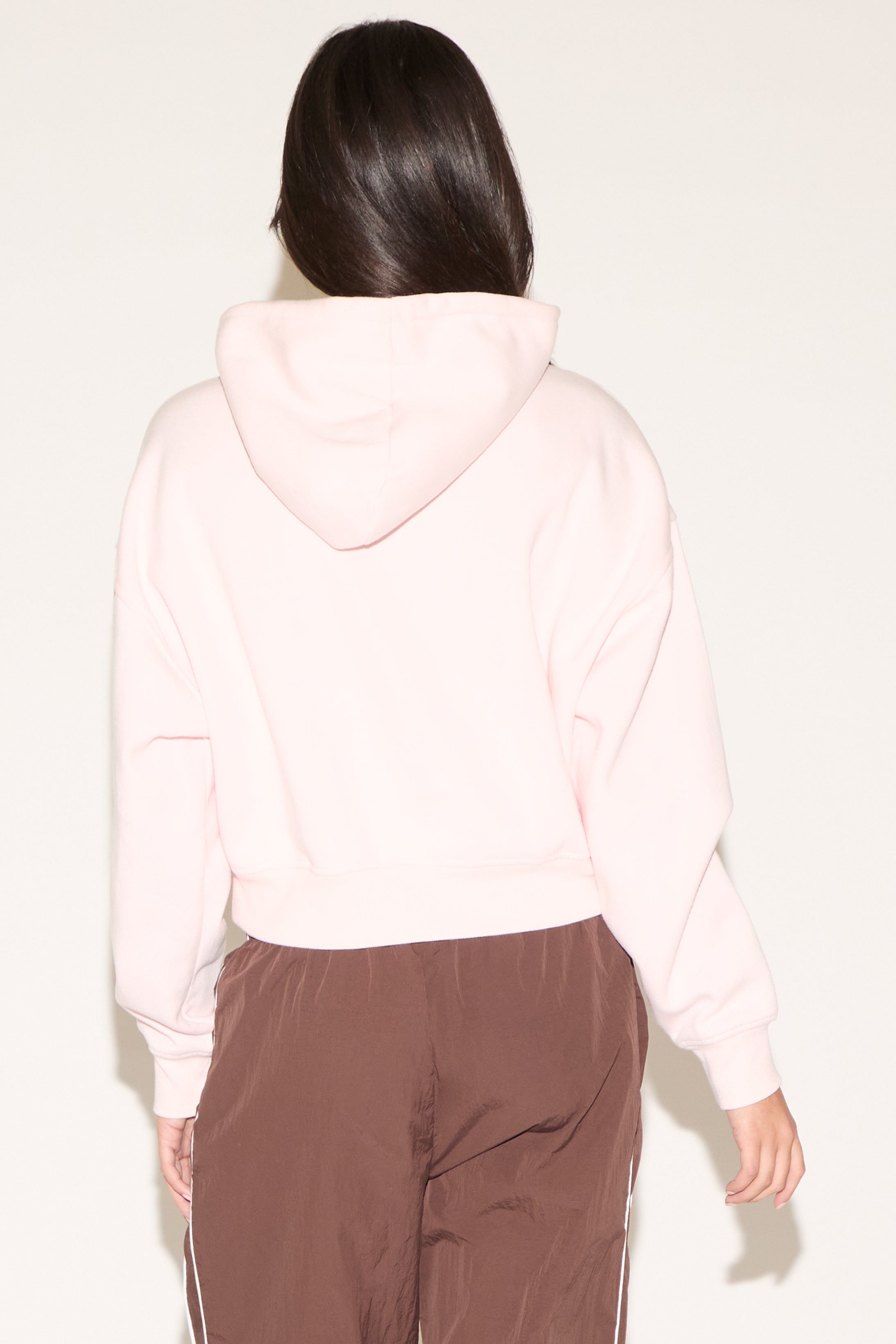 Person wearing a light pink hoodie and brown pants on a white background