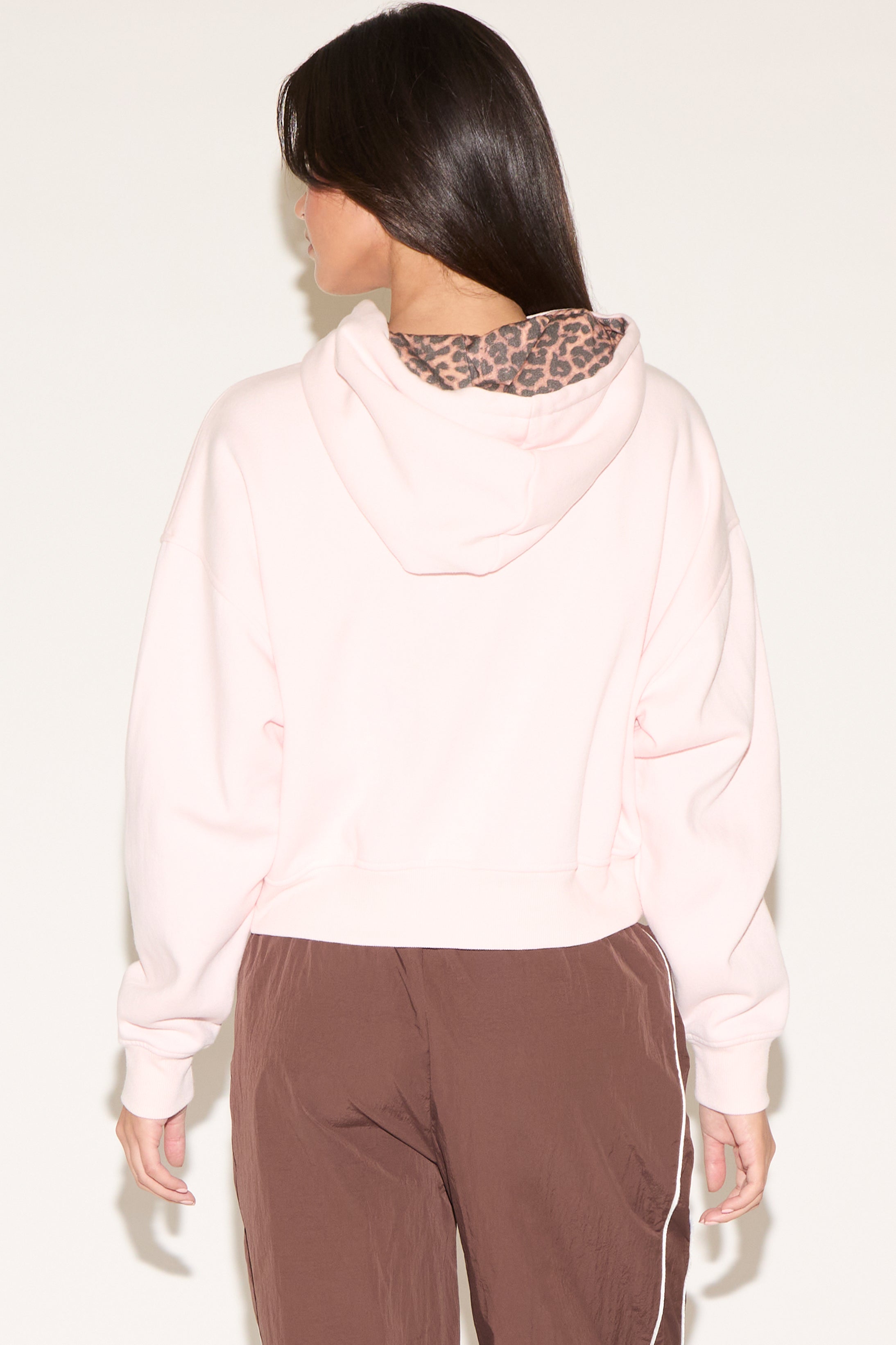 Person wearing a light pink hoodie and brown pants with a leopard print collar against a white background