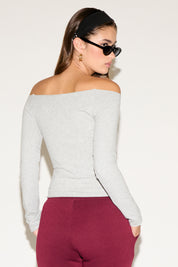 Woman wearing a light gray off-shoulder top and maroon pants against a white background