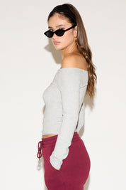 Woman wearing a gray off-shoulder top and maroon pants against a white background