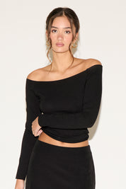 Woman wearing a black off-shoulder top against a plain background