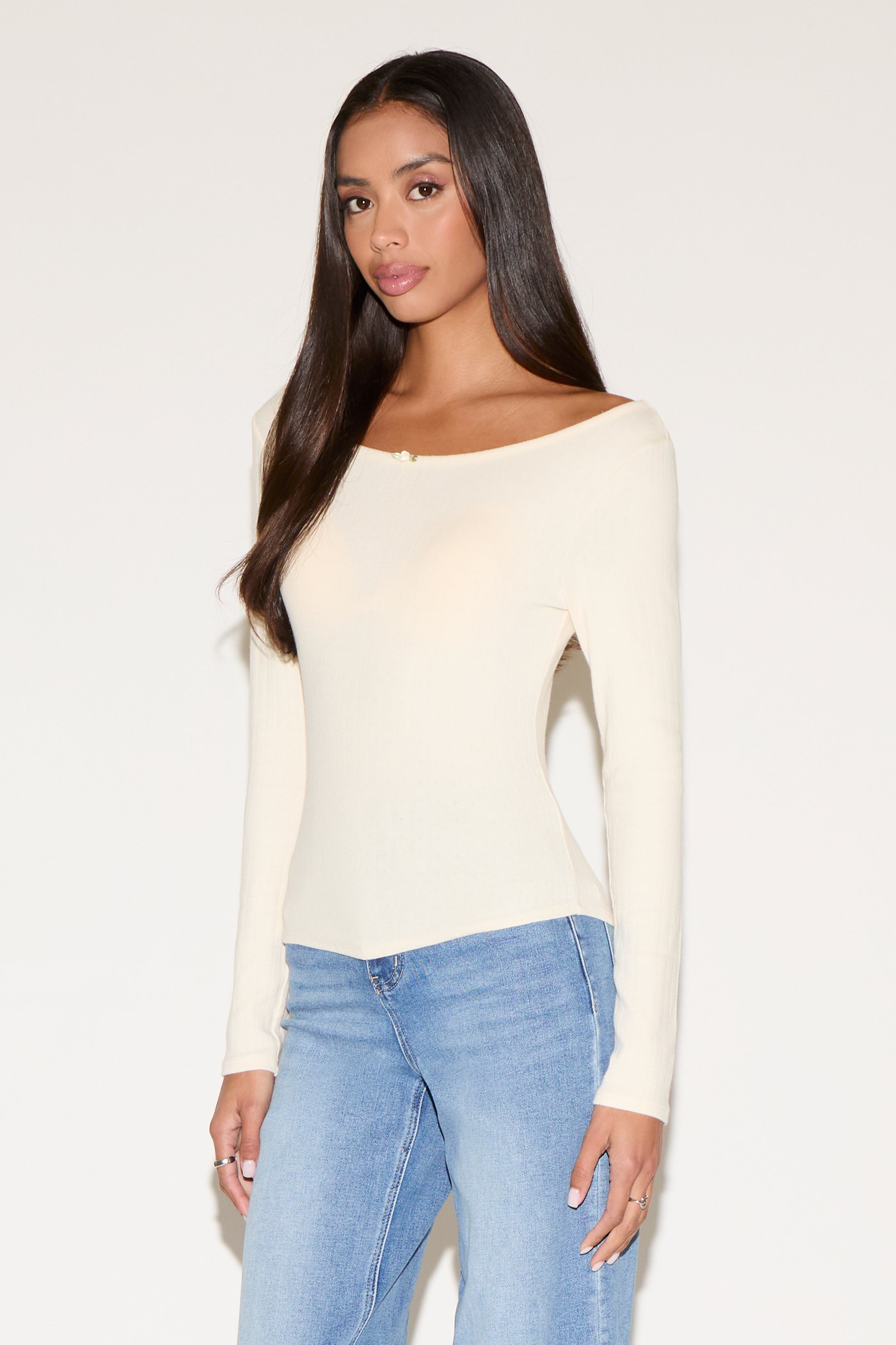 Woman wearing a cream long-sleeve top and blue jeans against a white background
